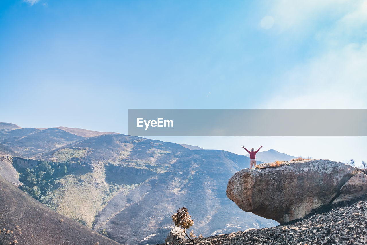 Rear view of woman with arms raised standing on mountain against sky