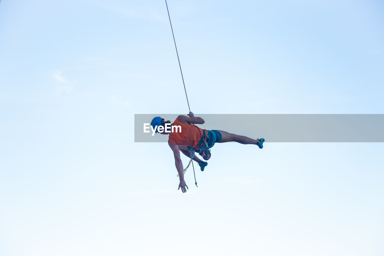 LOW ANGLE VIEW OF MAN CLIMBING ON ROPE AGAINST SKY