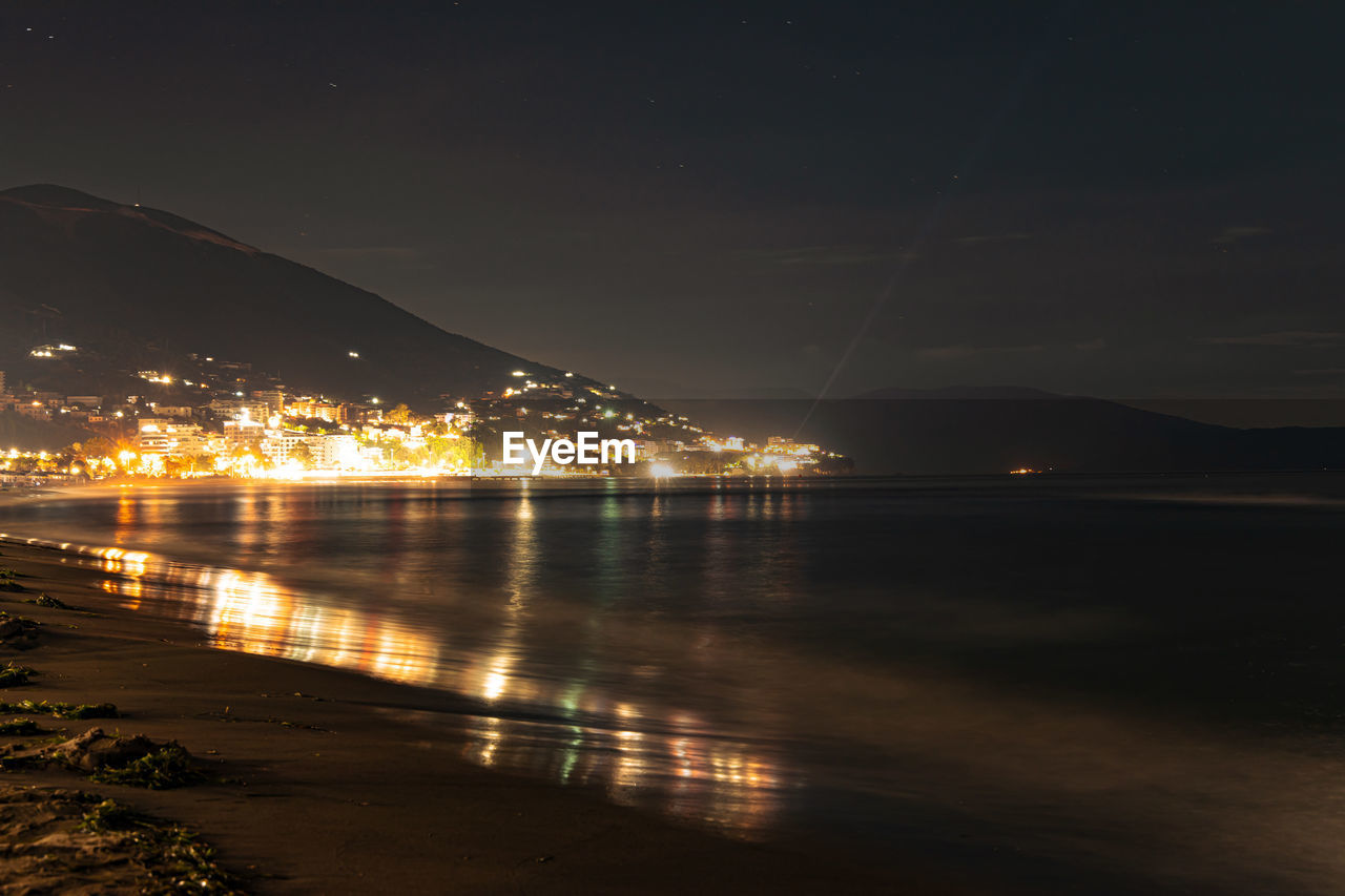 SCENIC VIEW OF ILLUMINATED CITY BY SEA AGAINST SKY