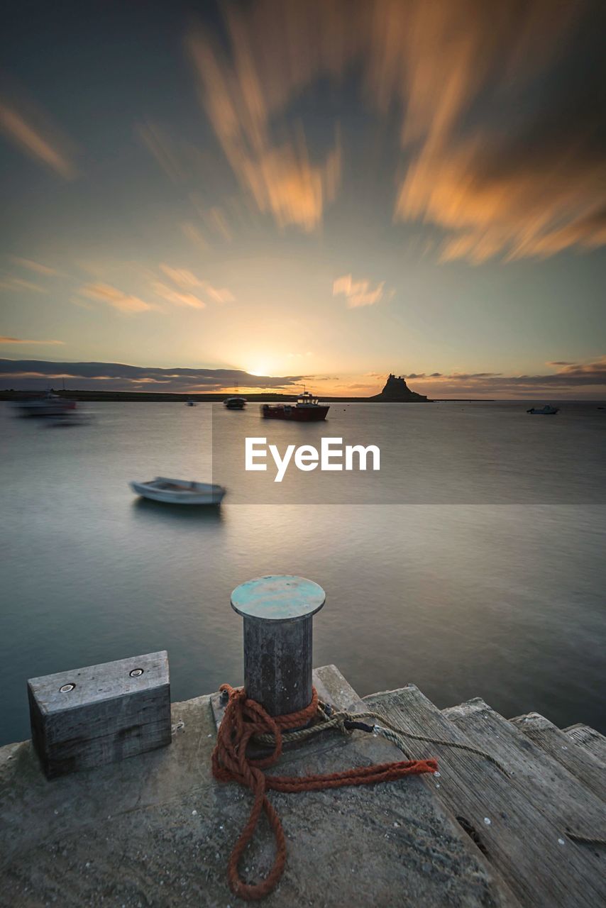 High angle view of rope tied to bollard by river against sky during sunset