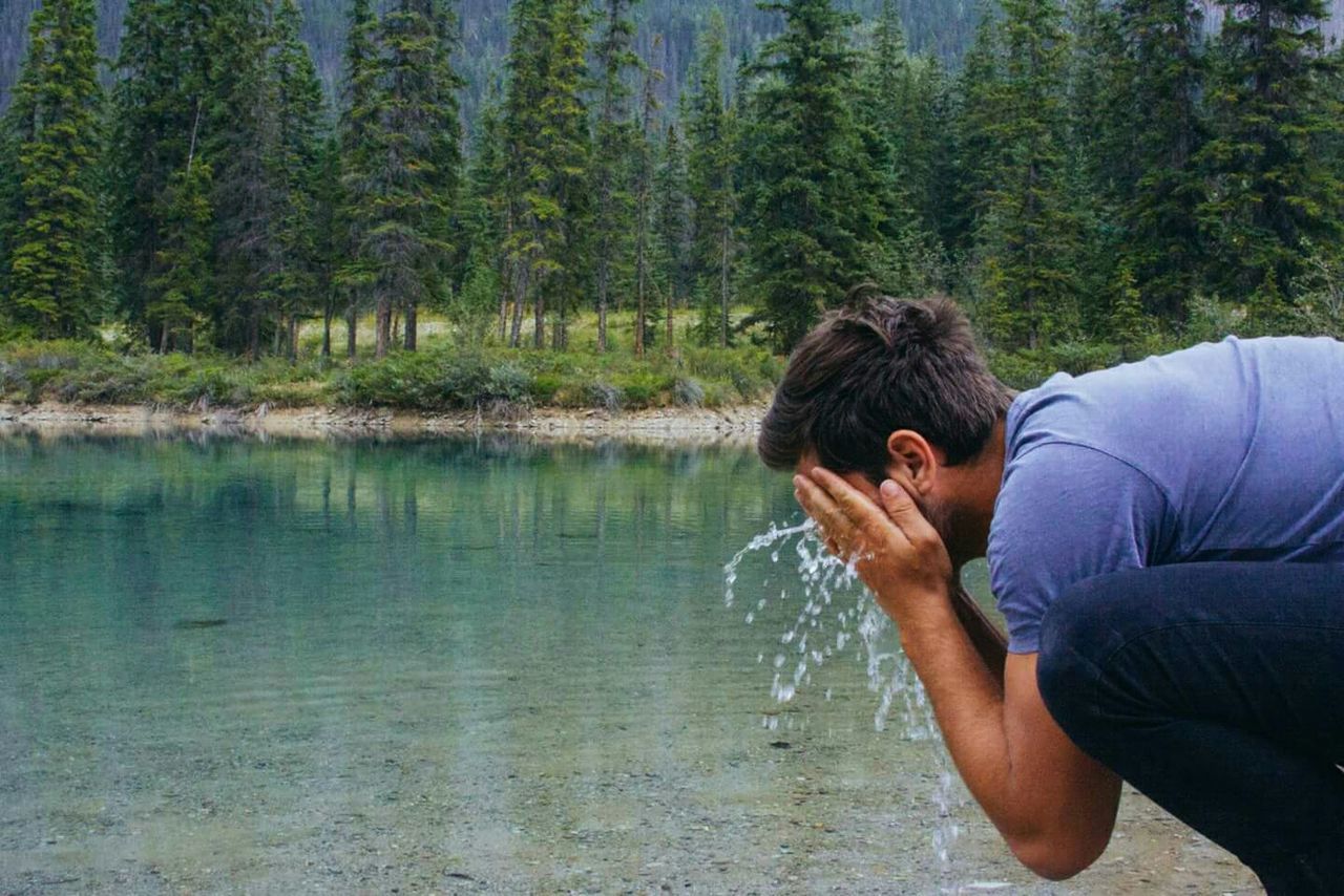 Side view of man splashing water on his face at lake