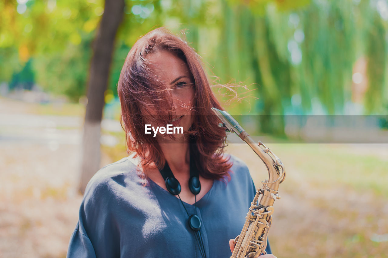 Beautiful red-haired girl in a blue jacket with a saxophone in windy weather