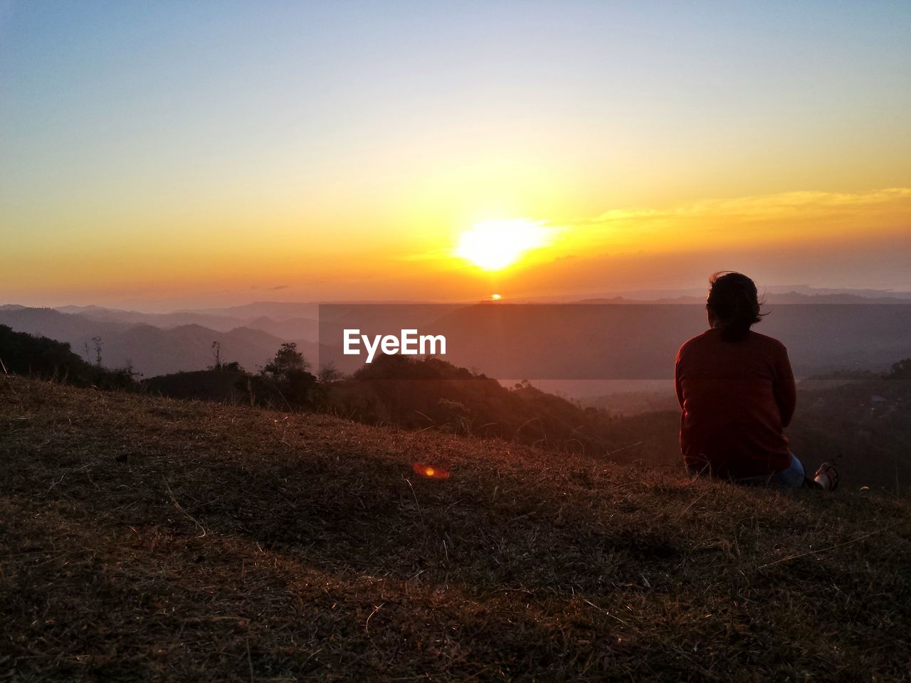 Rear view of woman sitting on mountain during sunset