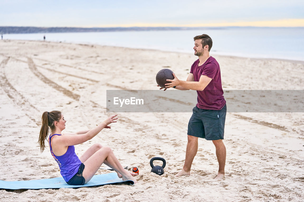 Friends exercising with medicine ball on sand at beach