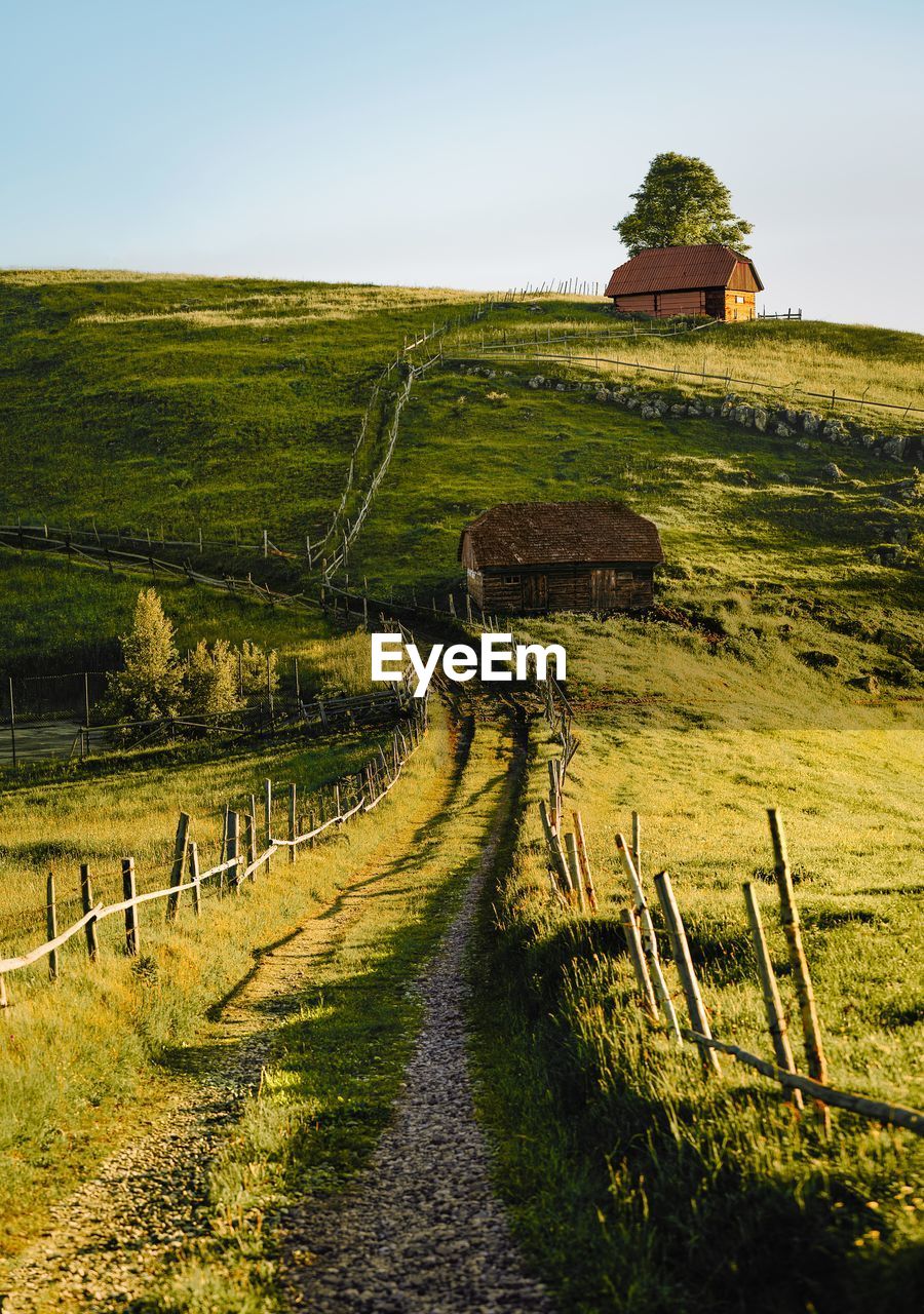 Scenic view of empty country road and house on hill against sky in summer