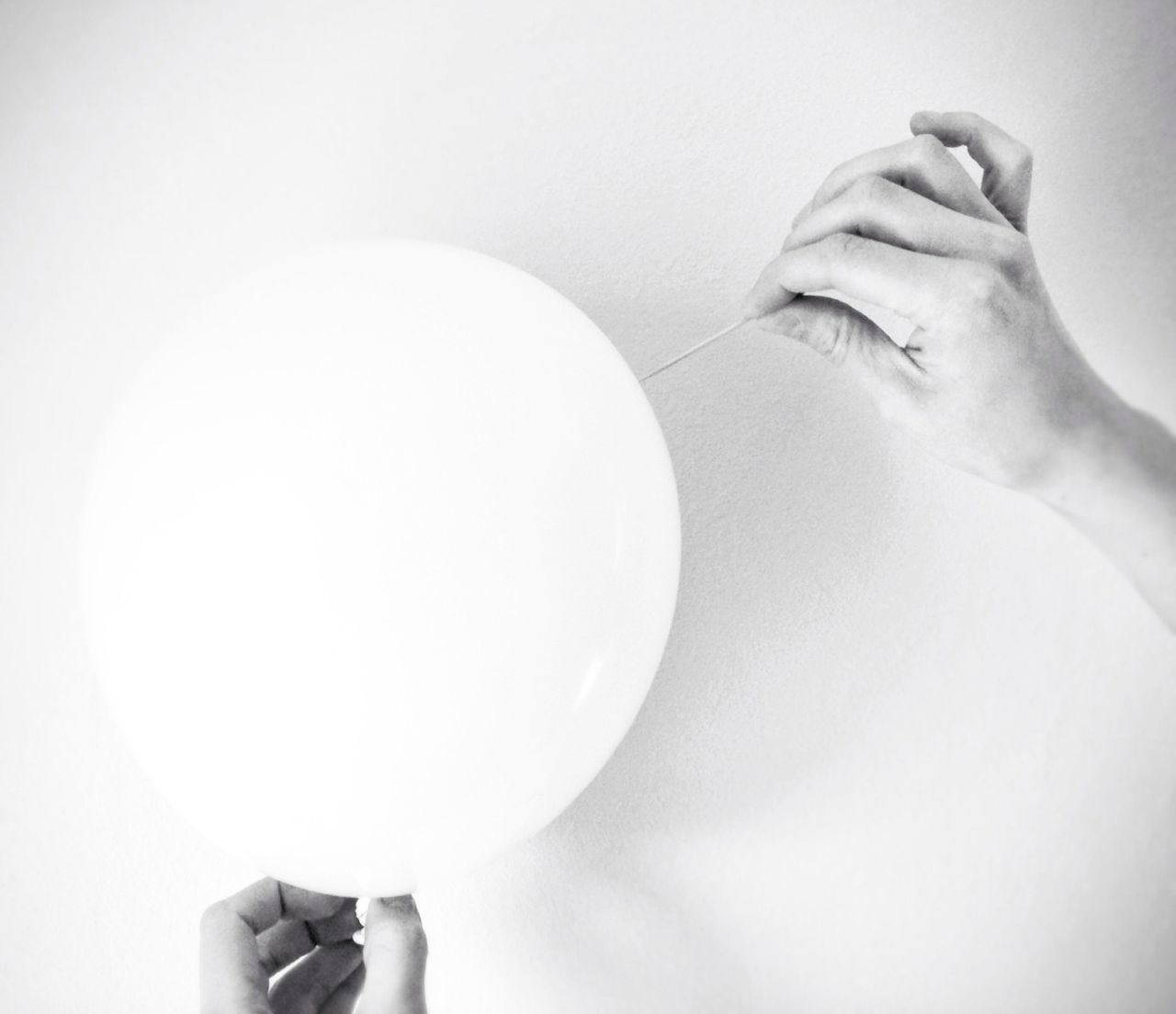 Close-up of hands holding balloon over white background