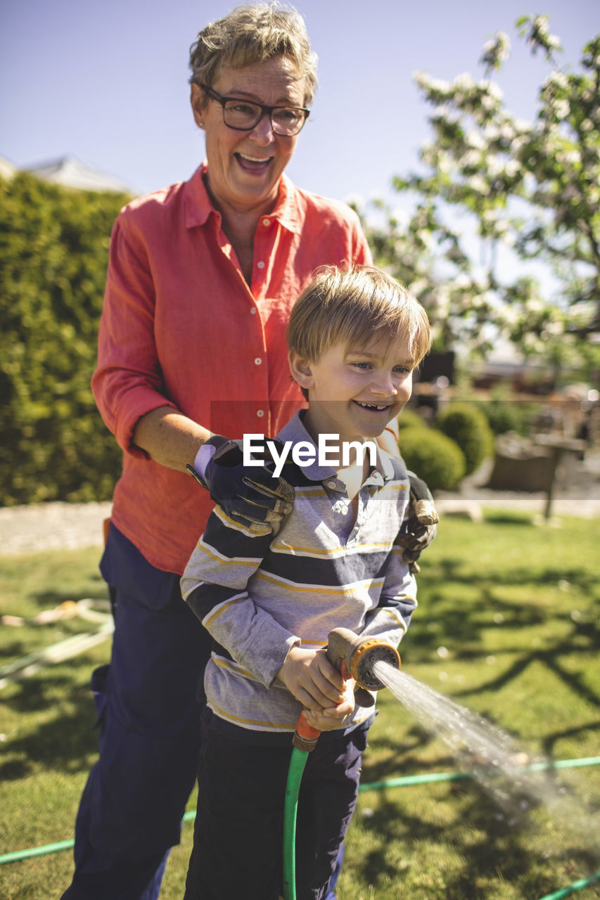 Happy grandmother and grandson spraying water in yard