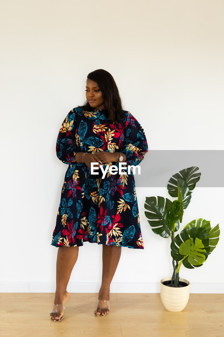 one person, full length, women, indoors, dress, clothing, standing, adult, fashion, spring, flower, portrait, pattern, studio shot, female, smiling, plant, front view, young adult, lifestyles, footwear, hairstyle, nature, houseplant, flowerpot, person, photo shoot, happiness, emotion, looking at camera, looking, holding