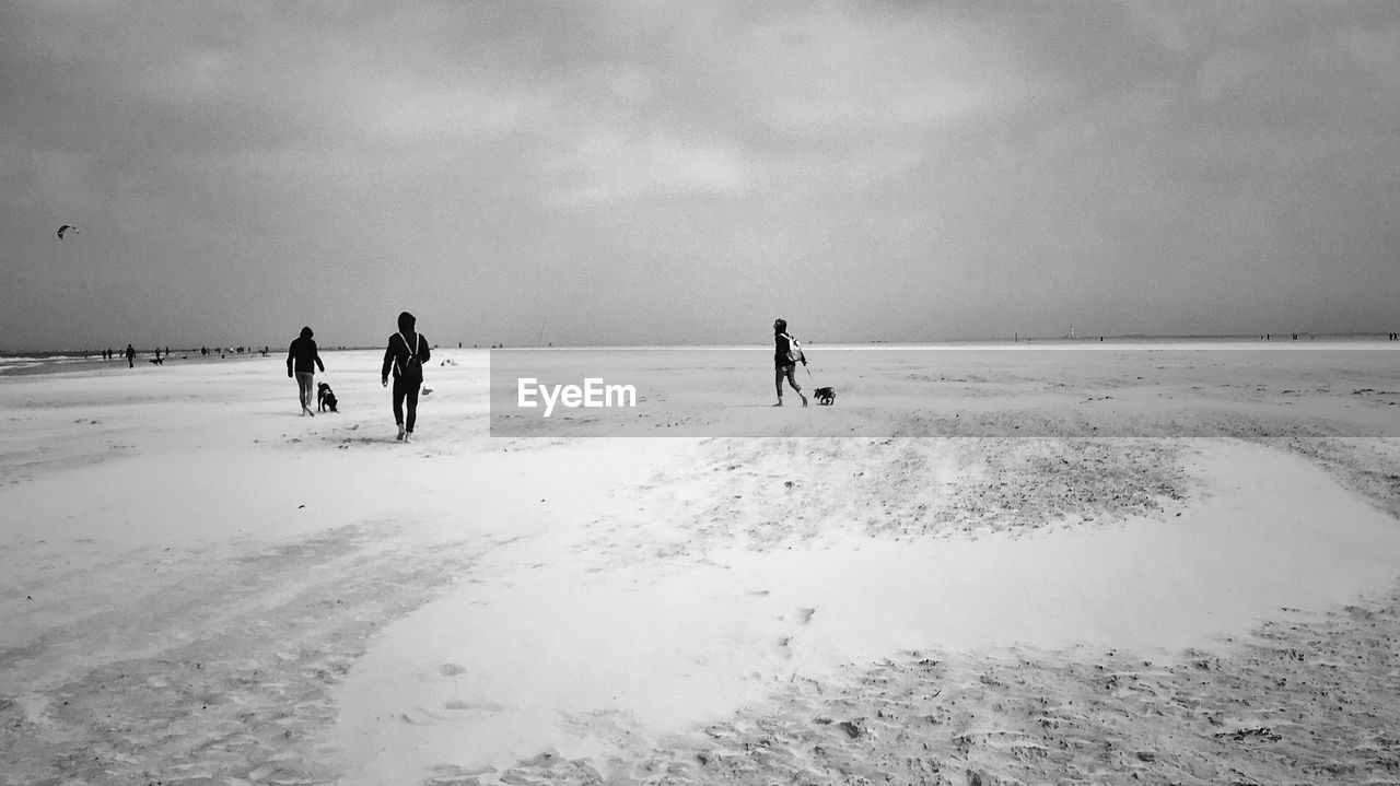 People walking on snow covered beach against cloudy sky