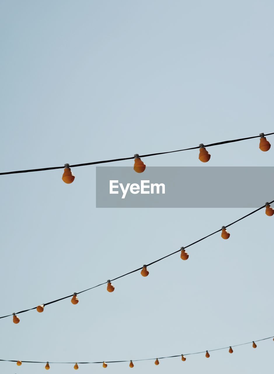 Low angle view of light bulbs hanging on cable against clear sky