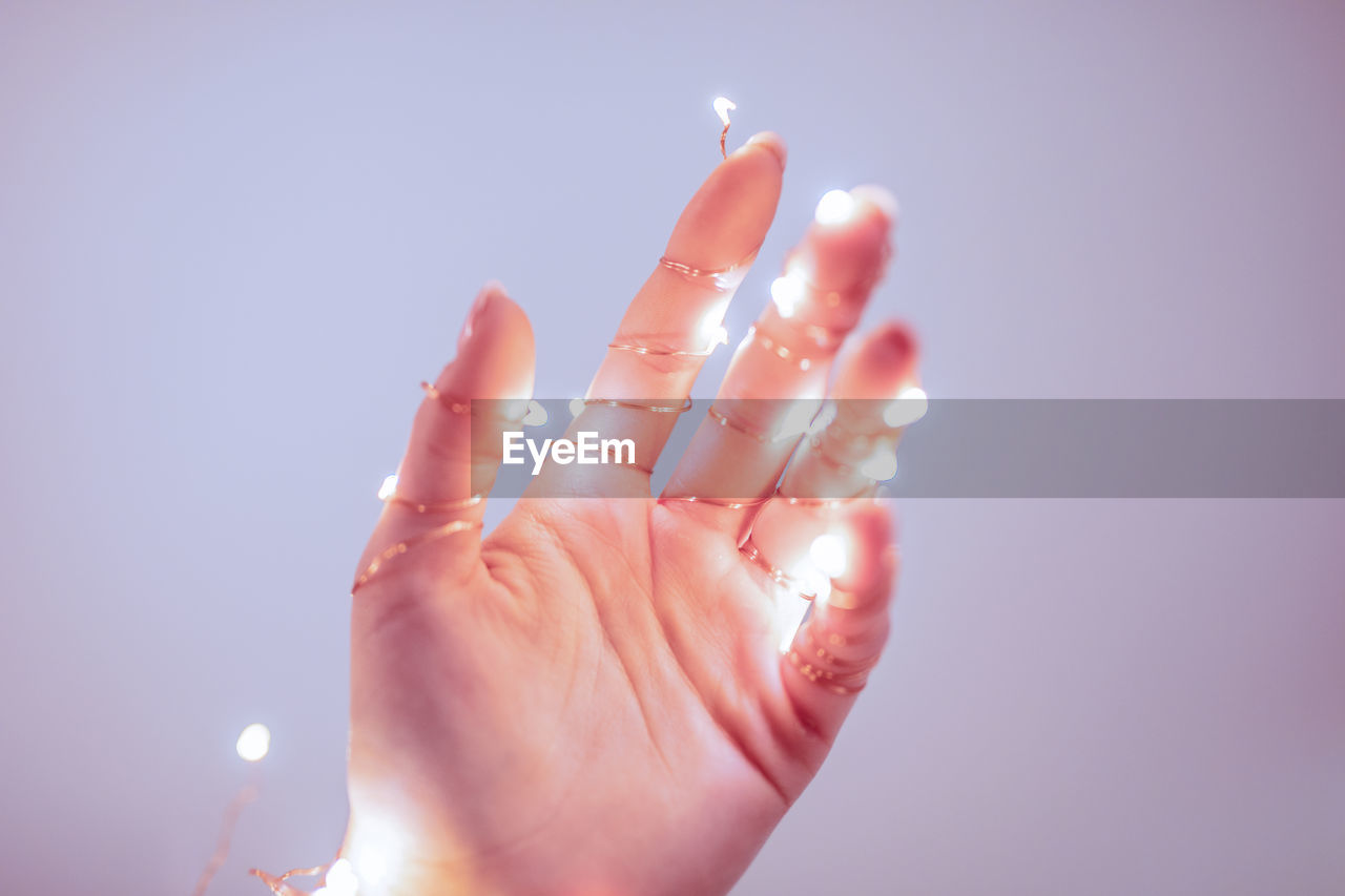 Close-up of hand wrapped in illuminated string light against purple background