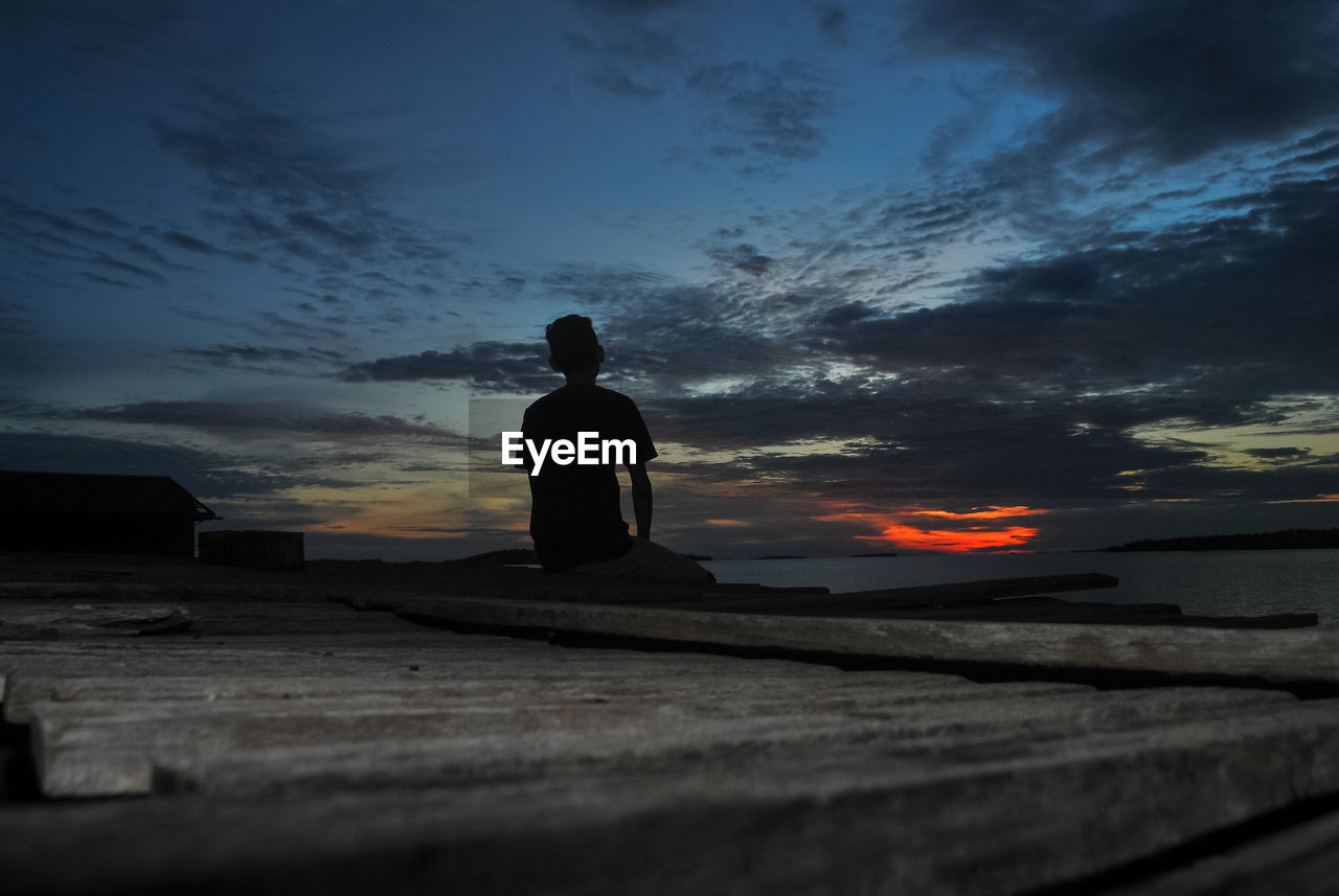 Rear view of silhouette man sitting at coast