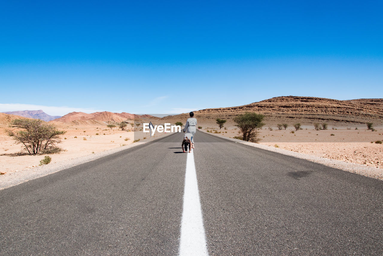 Full length of mother and daughter on road in desert during sunny day