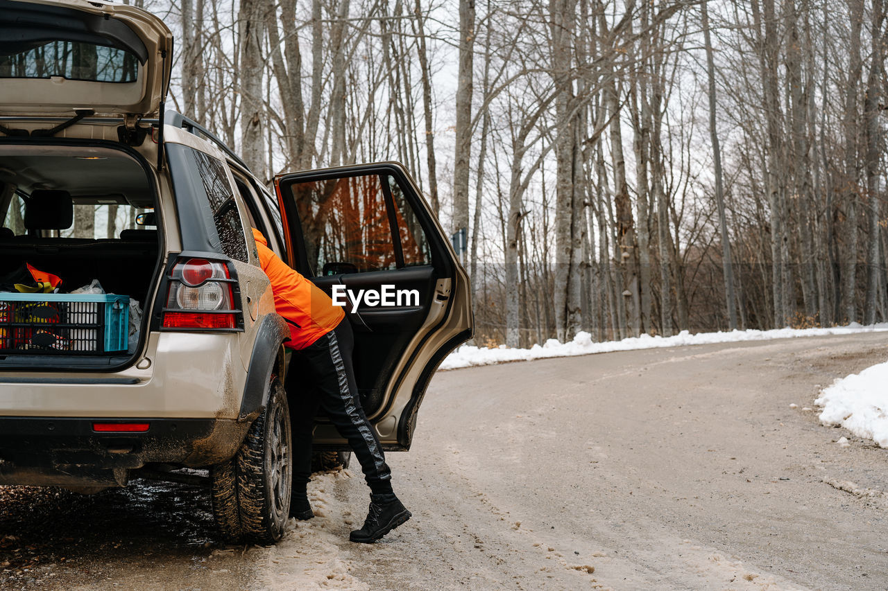 Man in car on snow covered road by bare trees in mountain during winter