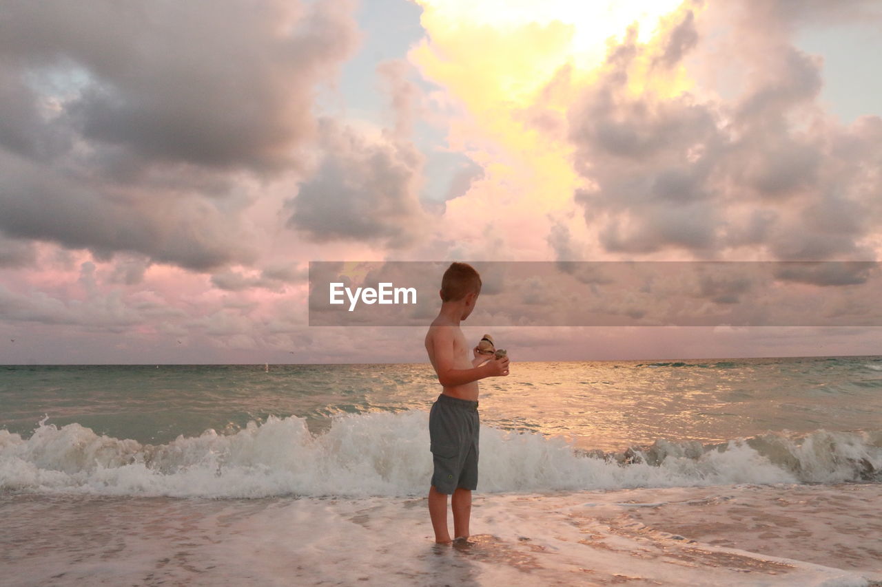 Boy standing on beach during sunset