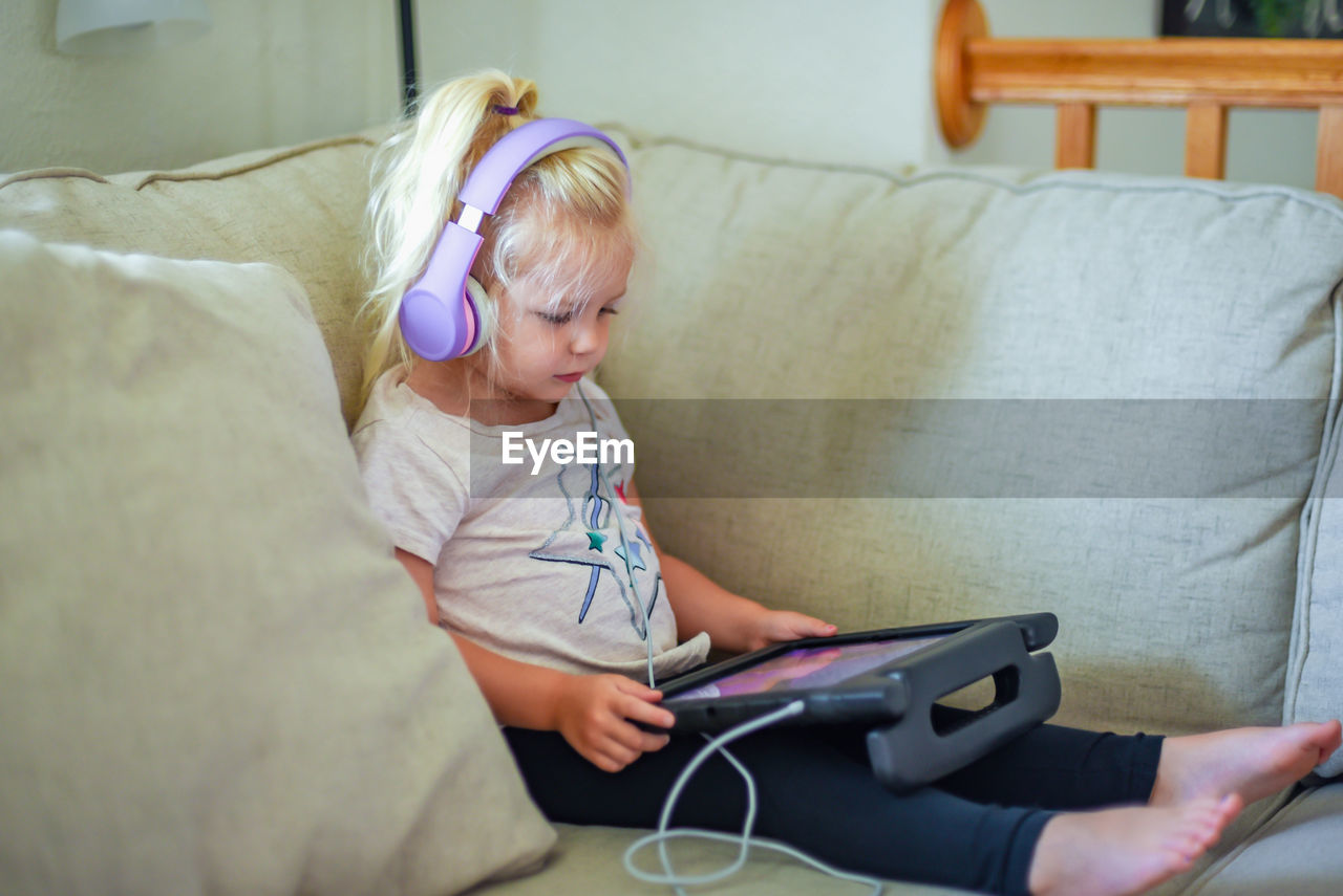 Girl using digital tablet while sitting on sofa at home