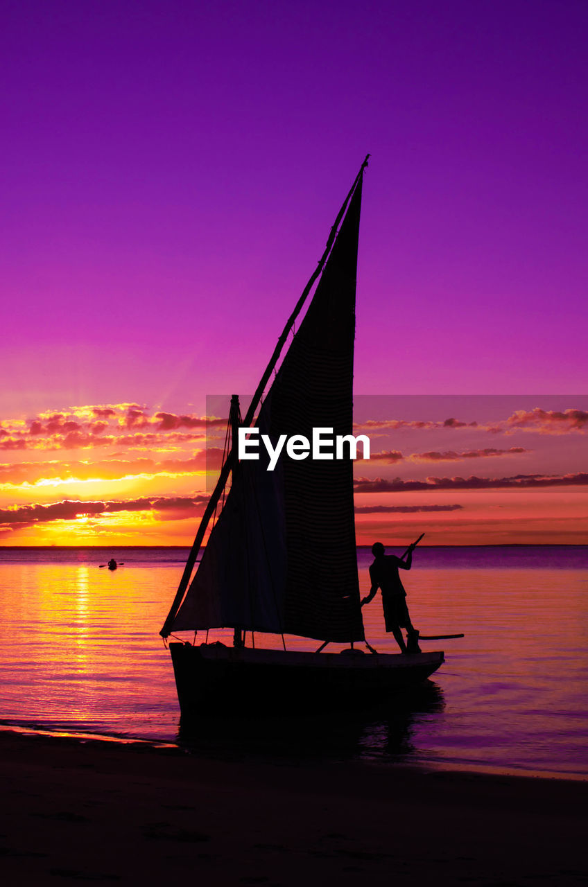 SILHOUETTE MAN ON BOAT AGAINST ORANGE SKY