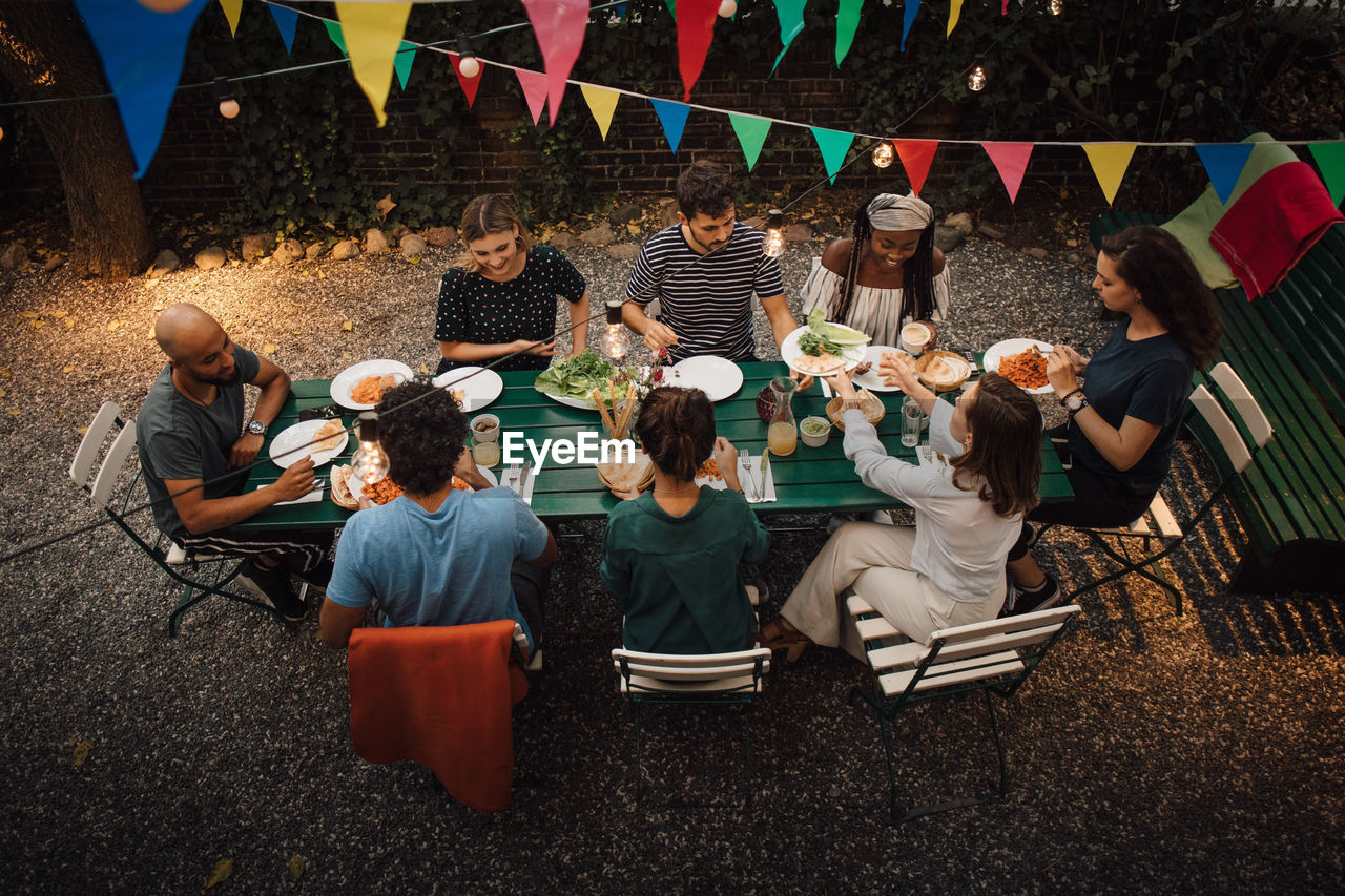 High angle view of multi-ethnic friends having food at table during dinner party in backyard