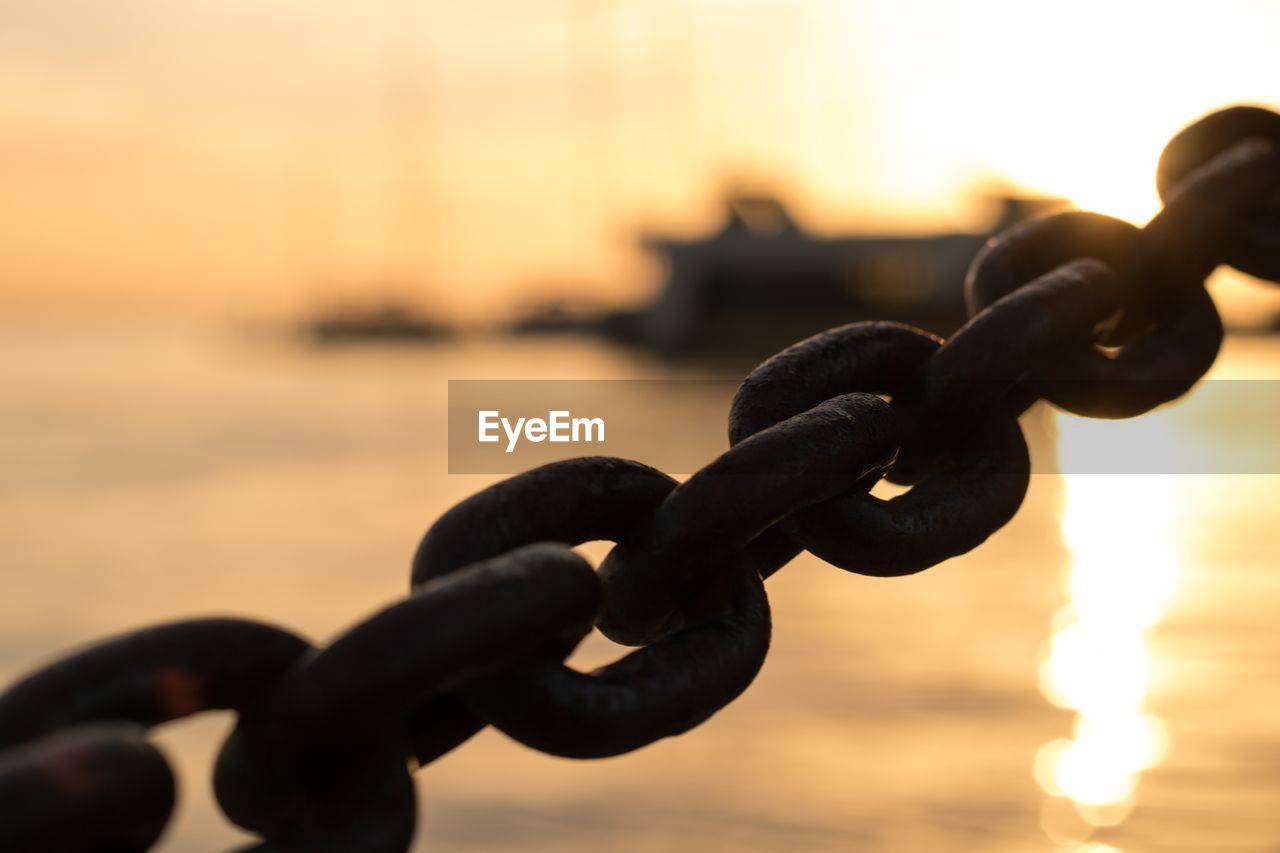 CLOSE-UP OF SILHOUETTE CHAIN AGAINST SEA DURING SUNSET