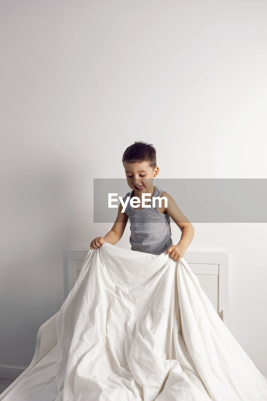 Child boy is mad having fun in a white bed in the children's room with a blanket