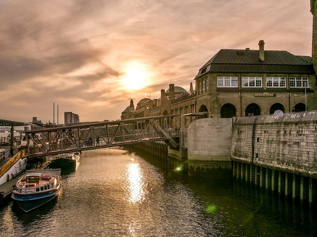 Bridge over canal by buildings against sky during sunset