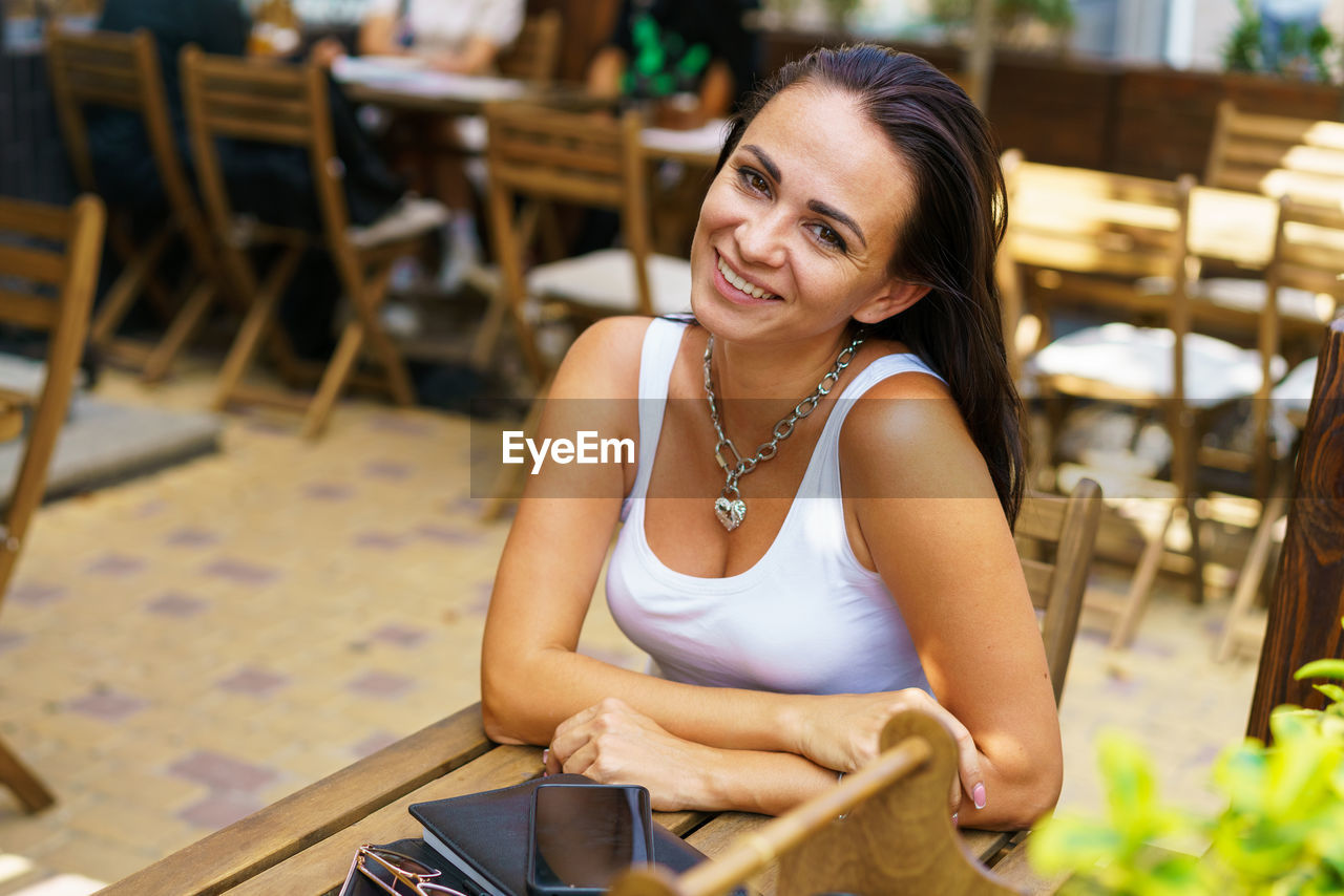 Satisfied young woman in white t-shirt sits at table of an outdoor street cafe.