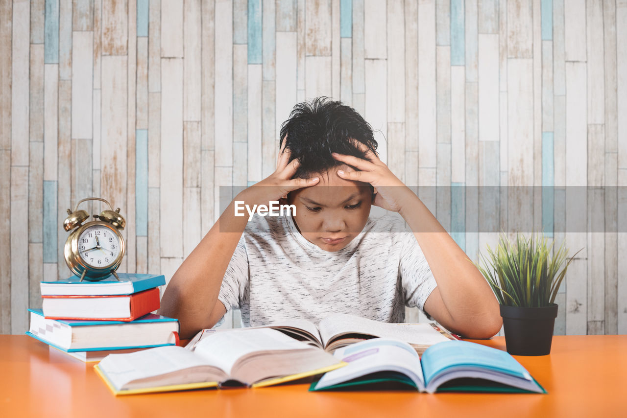 Frustrated boy sitting with head in hands by books on table