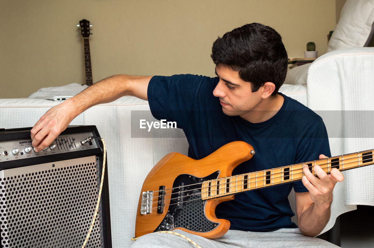 Man adjusting amplifier to play electric bass sitting at home.