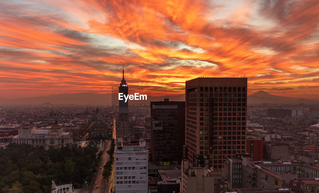 Buildings in city against romantic sky at sunset