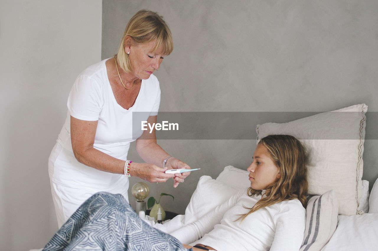 Grandmother examining granddaughter's temperature in bedroom