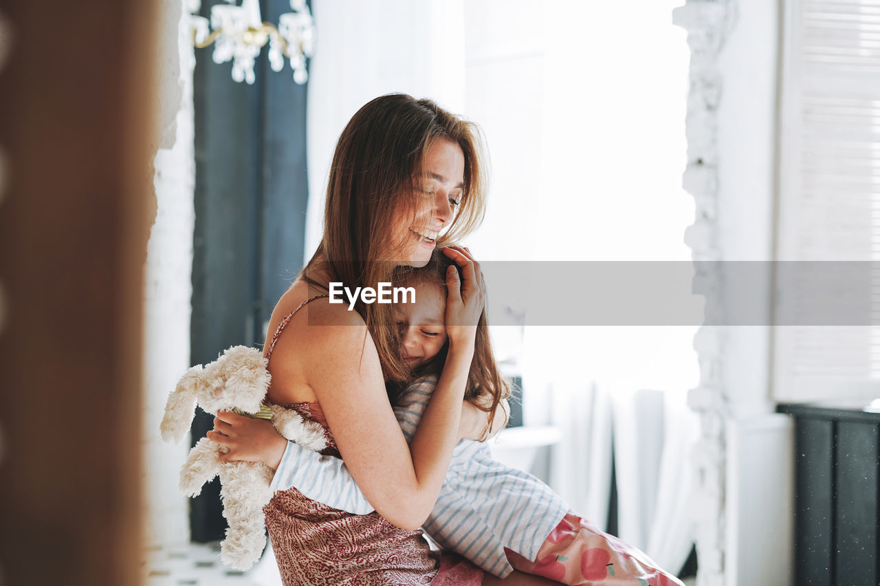 Young mother woman with long hair with little tween girl daughter in pajamas having fun in at home