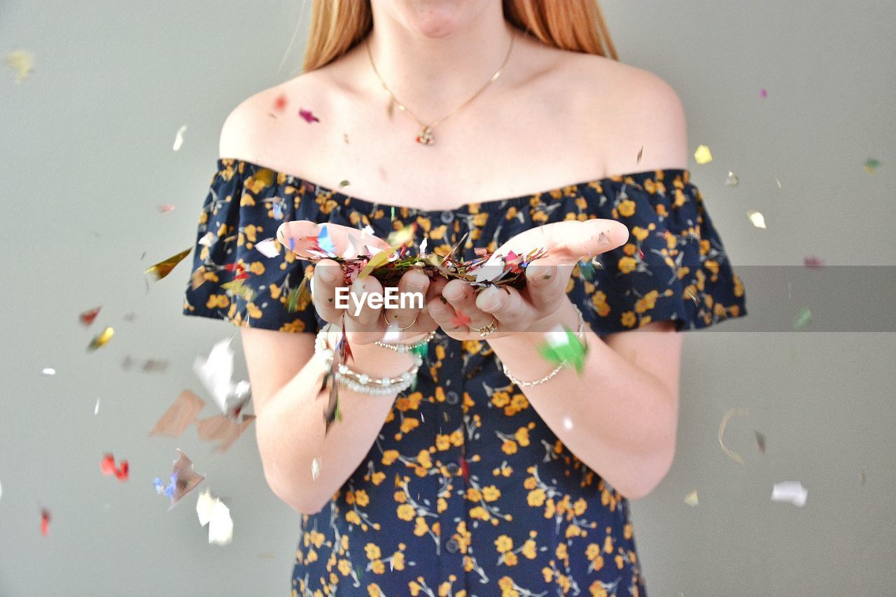 Midsection of woman blowing confetti against gray background