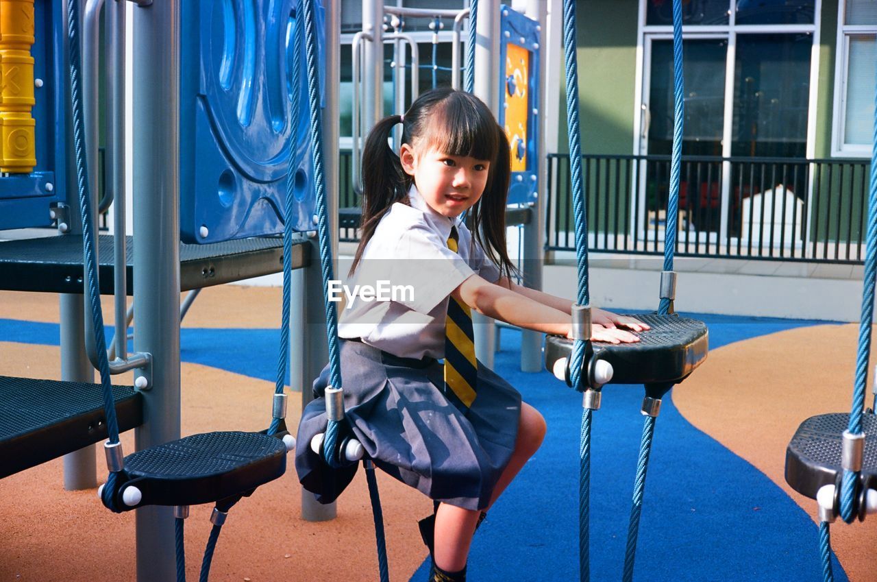 Smiling girl sitting on outdoor play equipment at playground