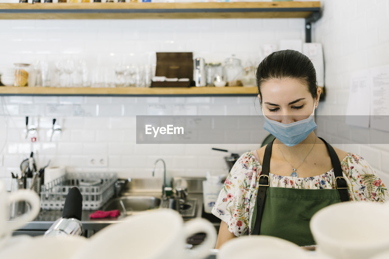 Woman wearing face mask while working in kitchen at coffee shop