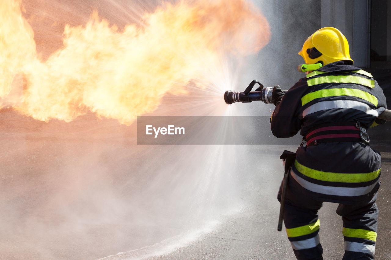 Rear view of firefighter spraying water on fire