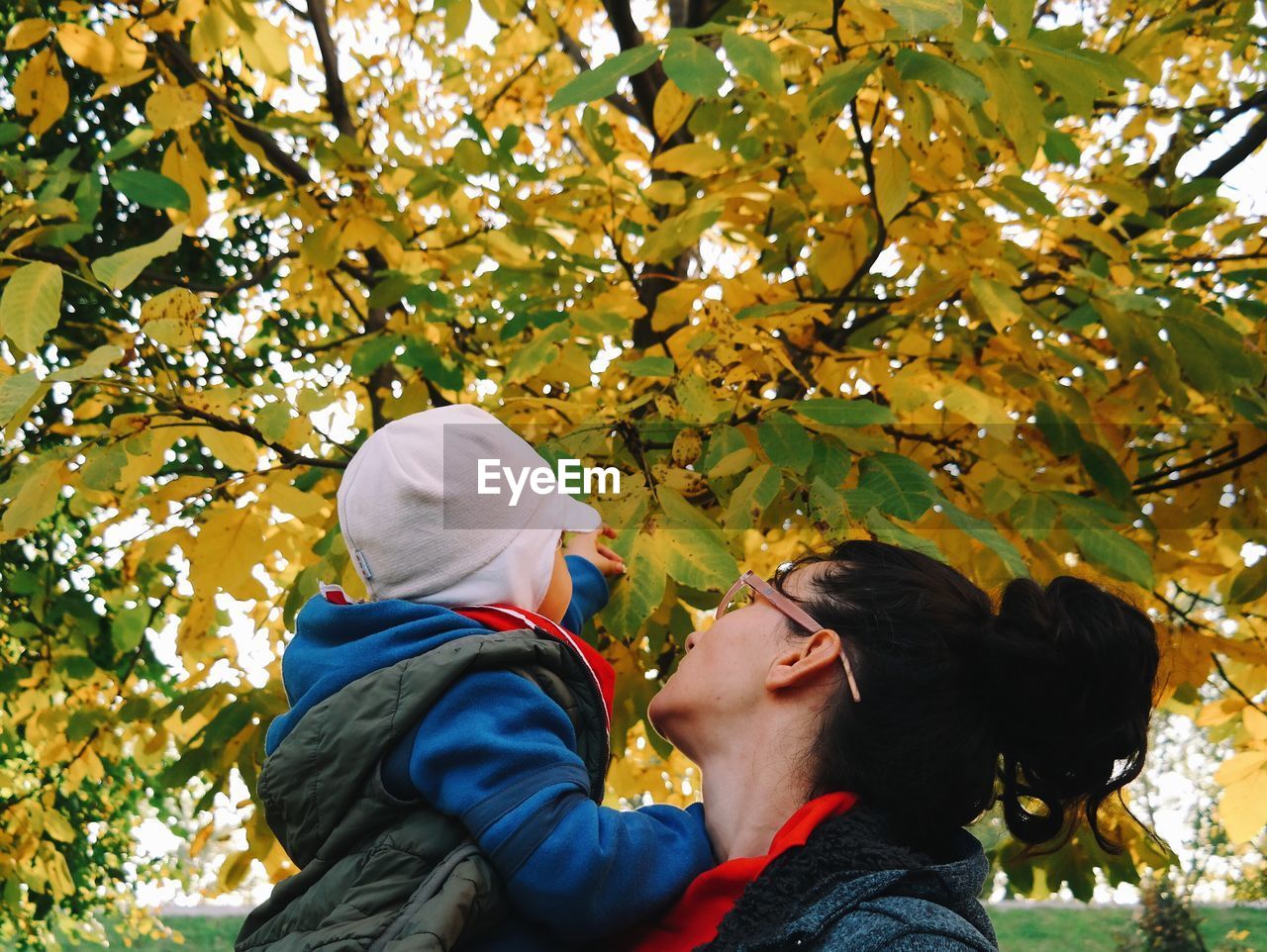 Low angle view of mother carrying son against tree in park