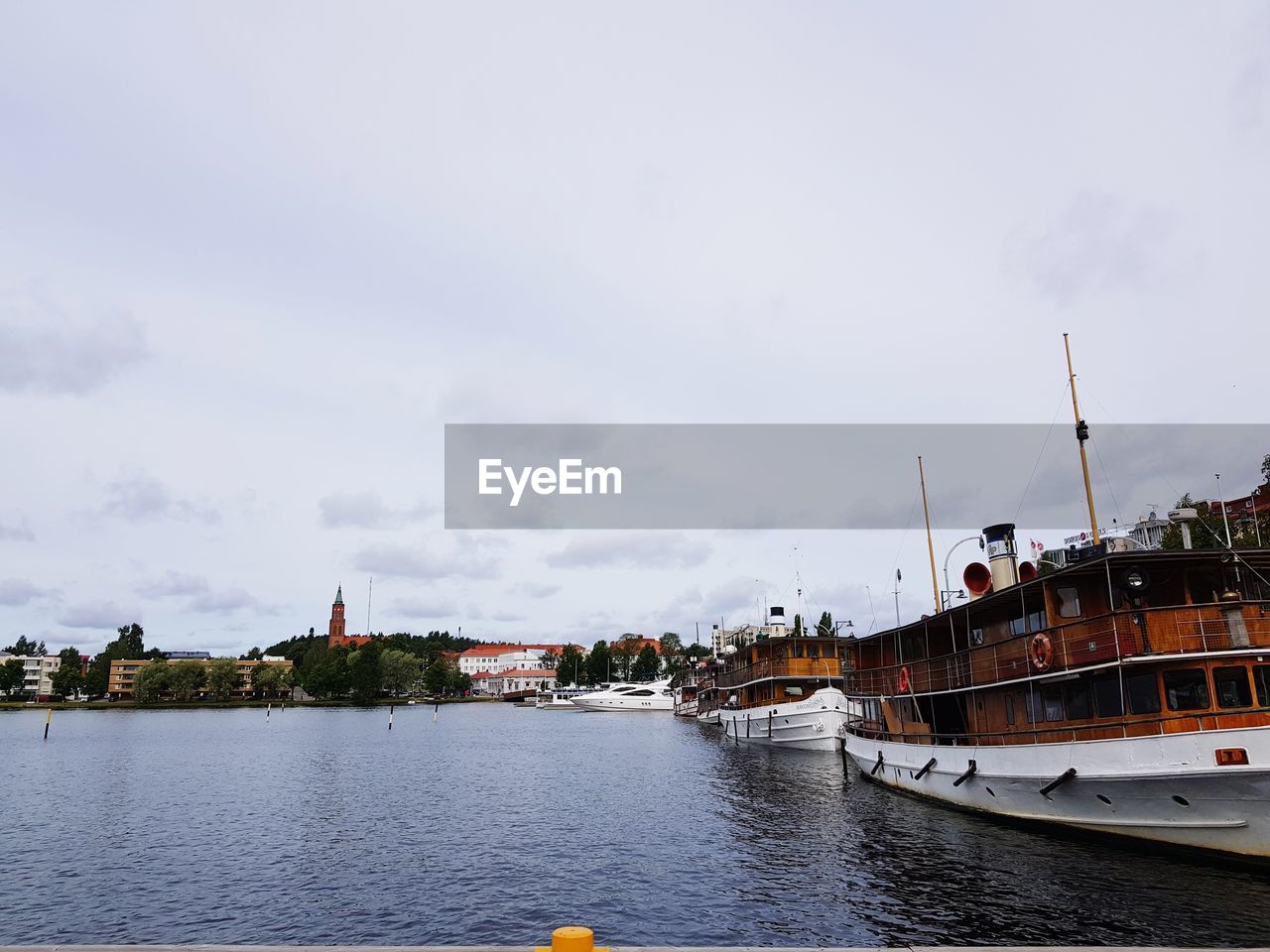 SAILBOATS MOORED ON RIVER BY BUILDINGS AGAINST SKY IN CITY