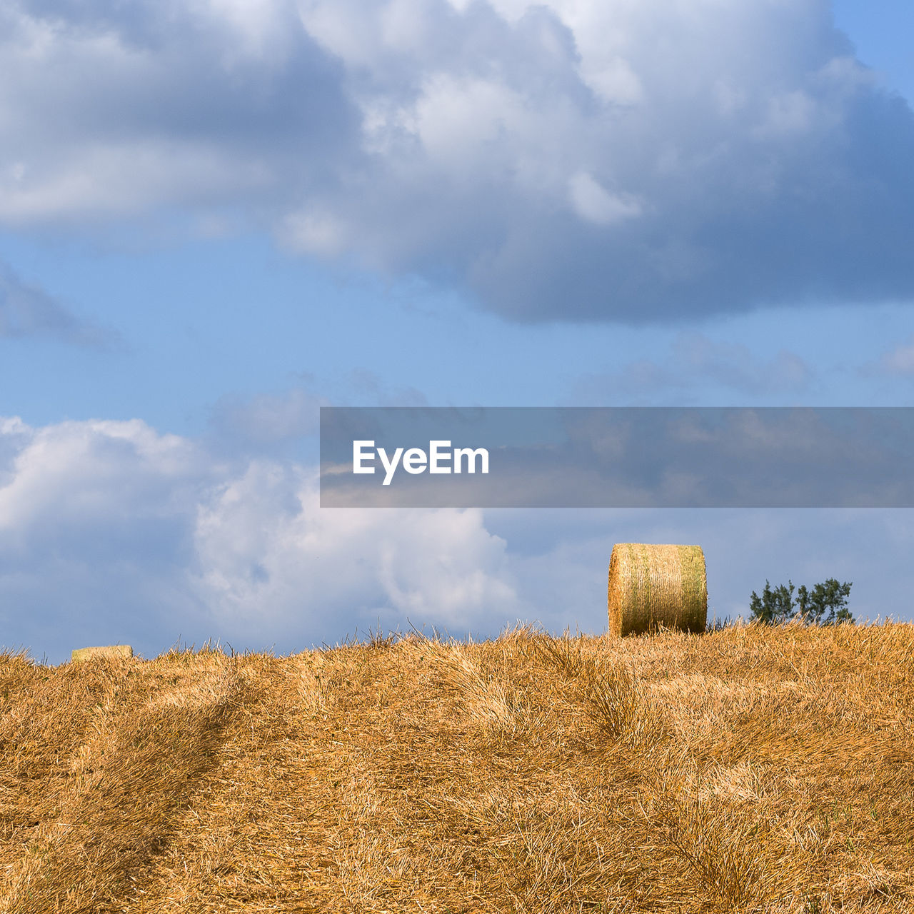 Hay bale on field against cloudy sky
