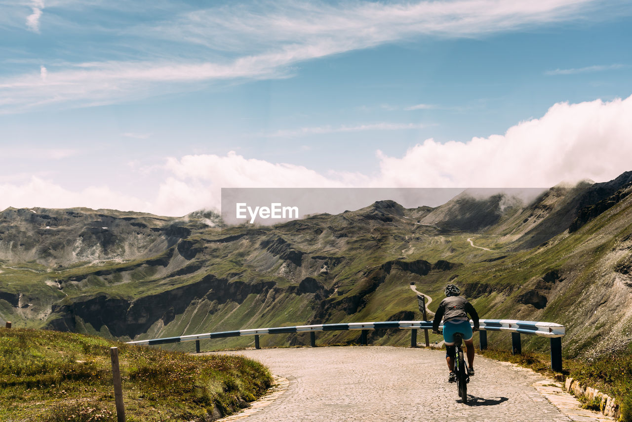 Woman riding bicycle on mountain road against sky