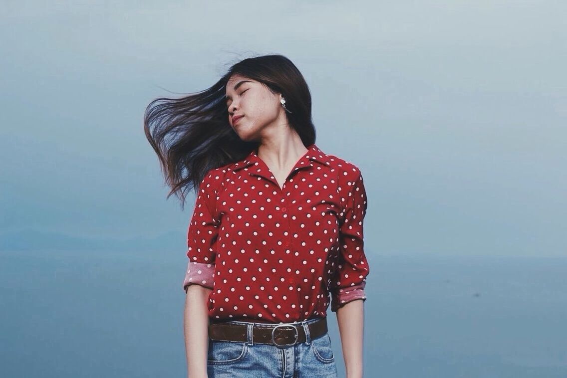 YOUNG WOMAN STANDING AGAINST RED BACKGROUND