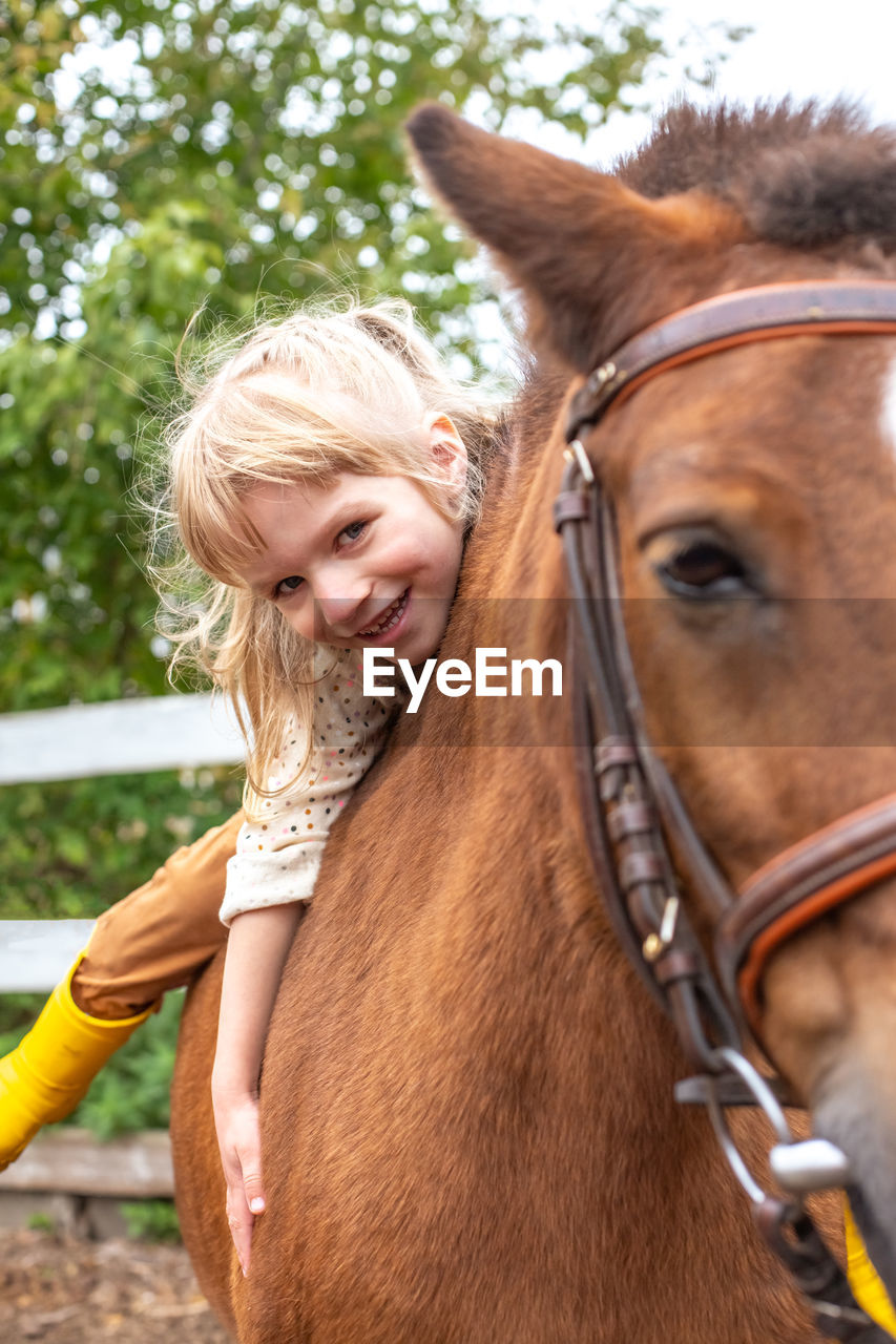 Little girl hugs pony horse and laugh happily