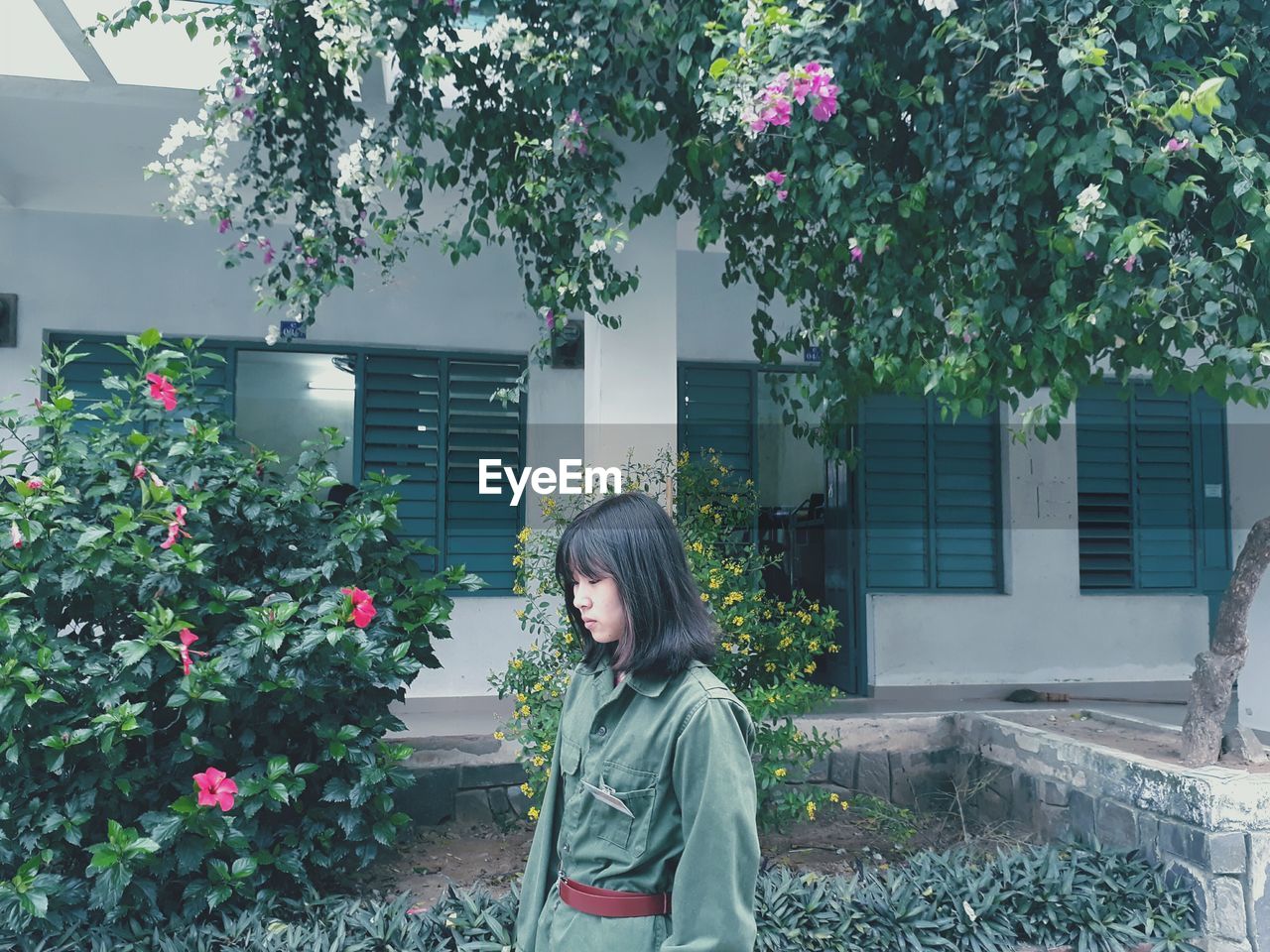 Woman wearing military uniform while standing by plants against building