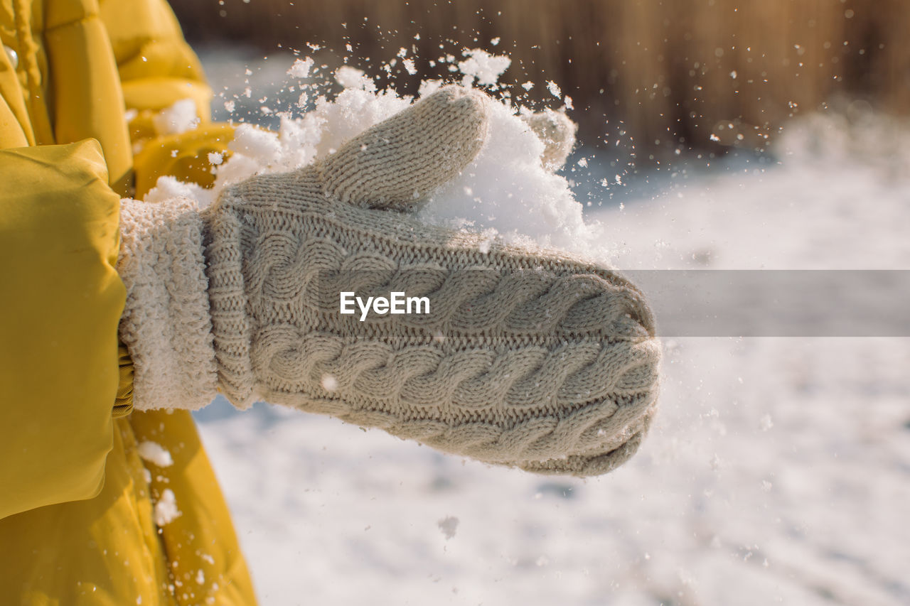 Midsection of person holding snow in woolen gloves