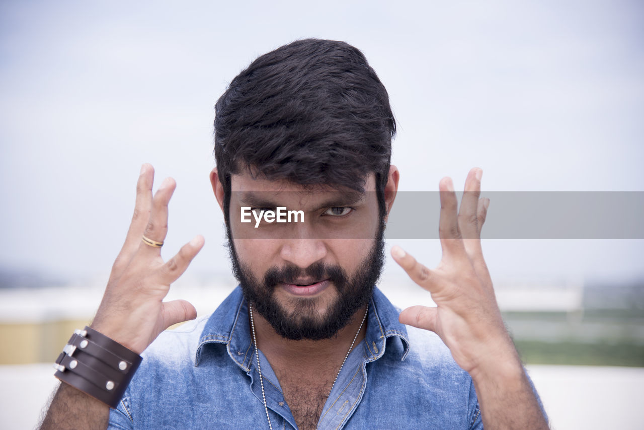 Portrait of serious man gesturing against sky