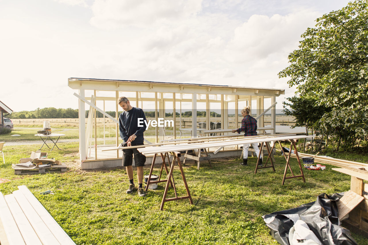 Man and woman making shed at farm against sky