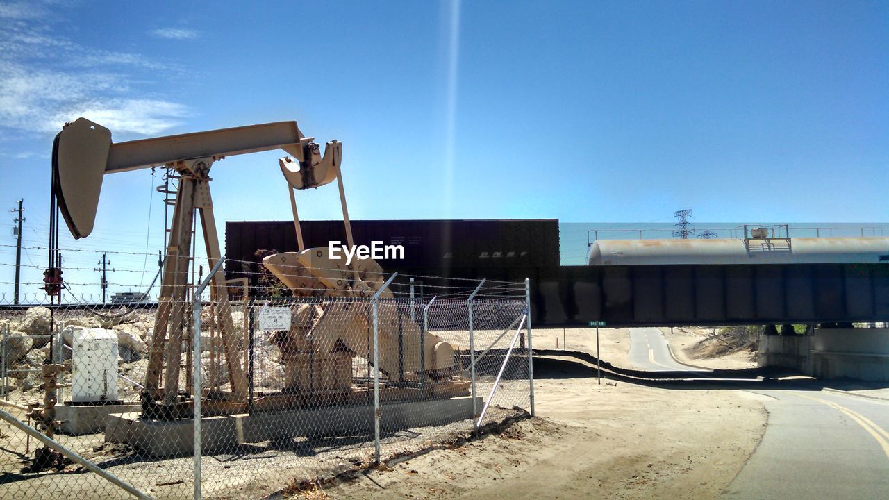 Oil machinery by freight train against sky