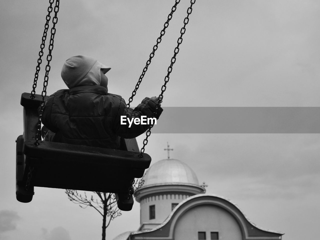 Rear view of boy swinging in playground against sky