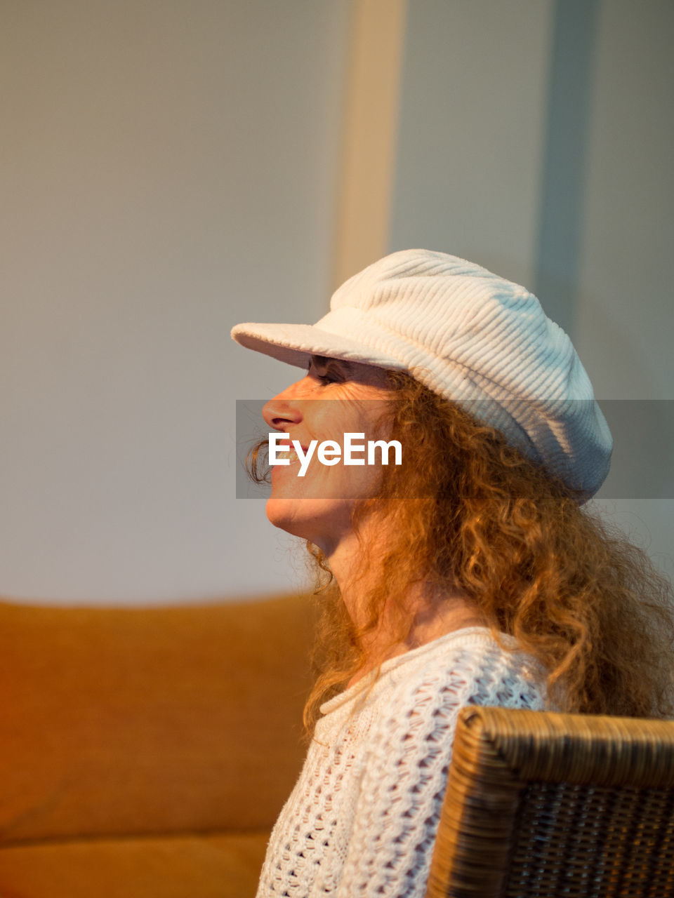 Profile view of smiling woman wearing hat sitting on chair at home