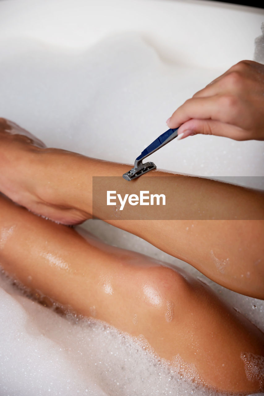 Midsection of woman shaving leg in bathtub