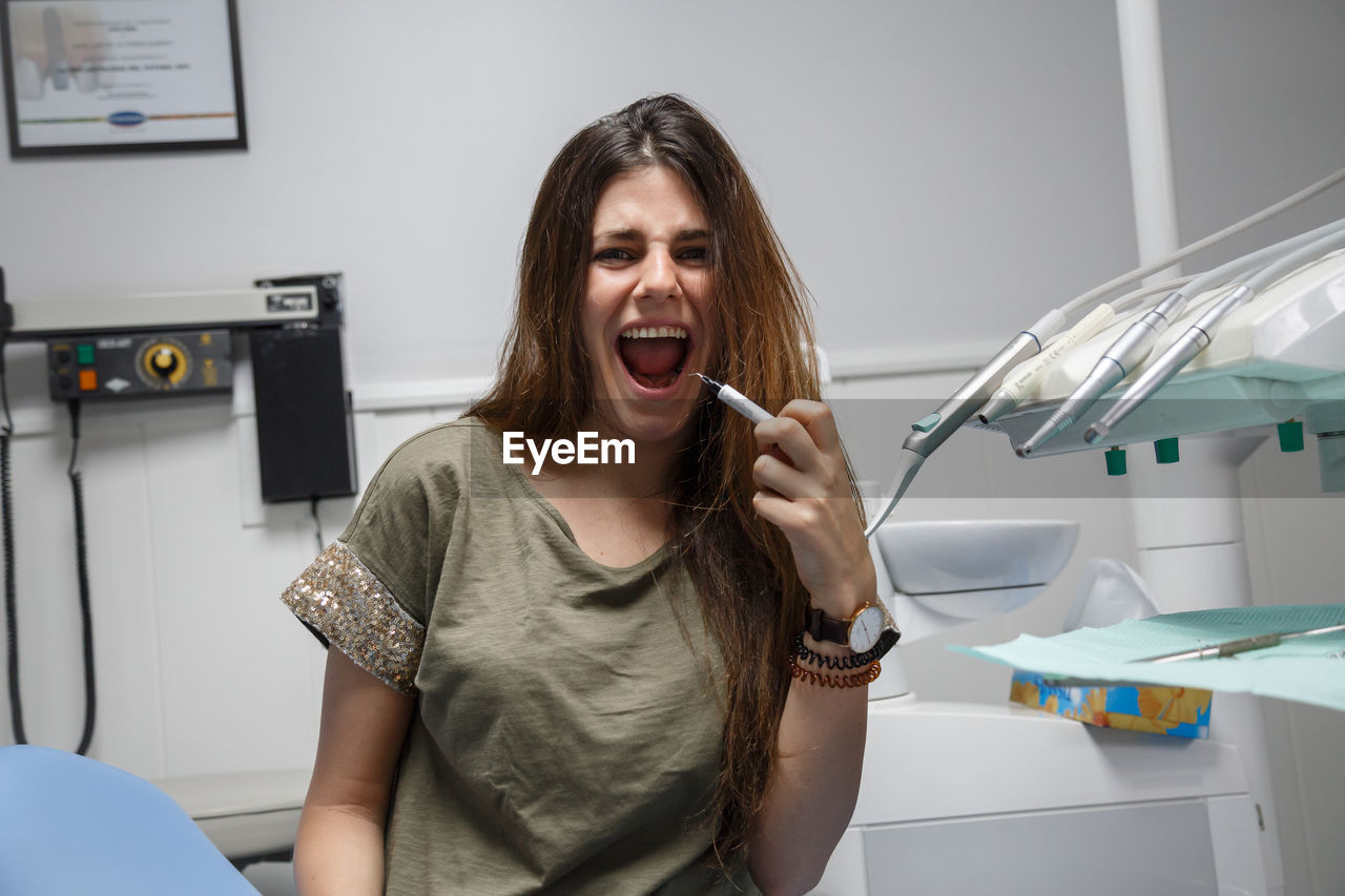 Portrait of young woman sitting in the chair of a dental clinic making faces.